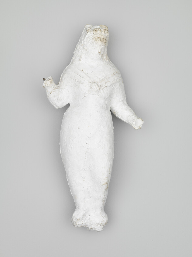 A small white plaster sculpture of a standing humanoid animal with raised arms.