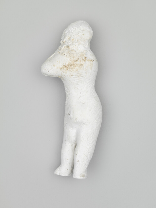 Small white plaster figurine of a standing human figure with arms raised toward its head.