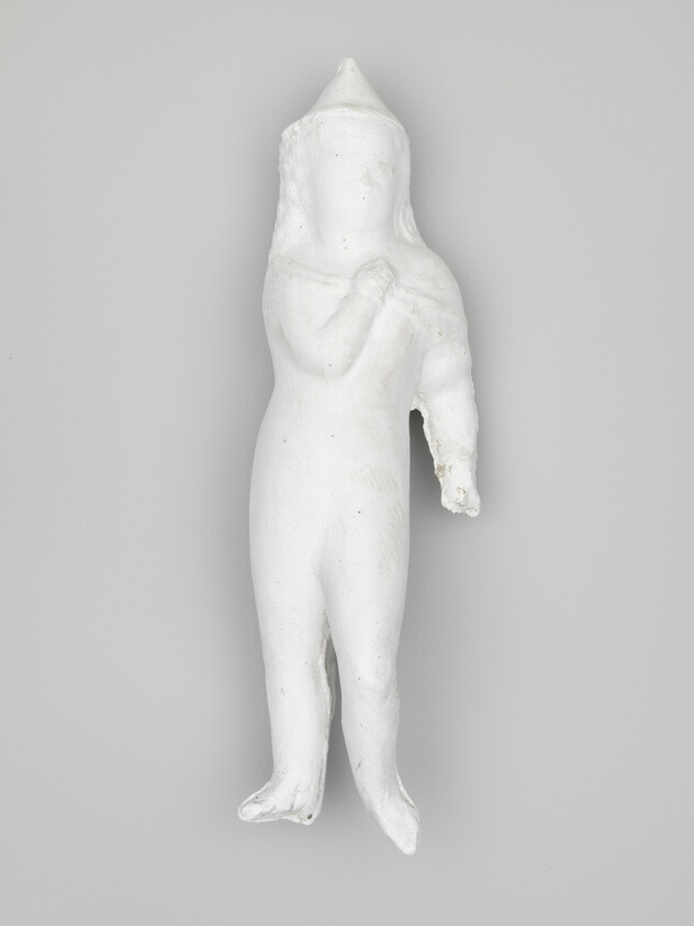 White plaster doll with a cone hat and a broken right arm hanging on a gray wall.