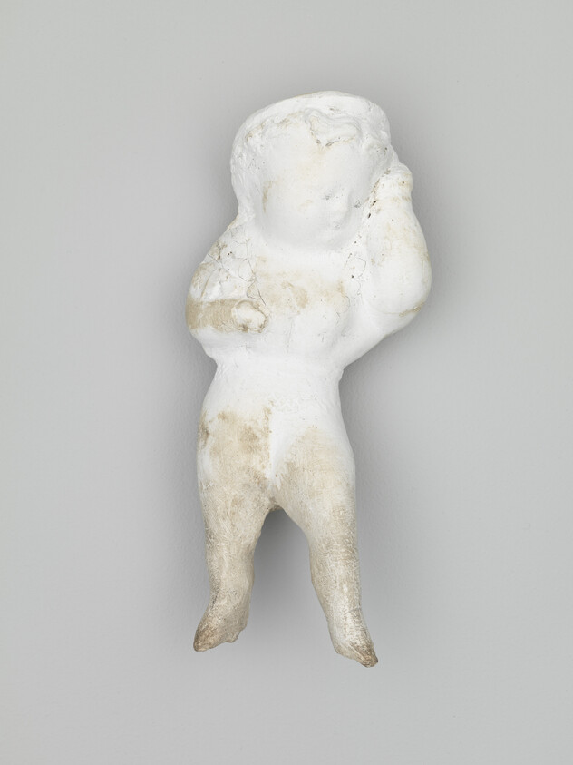 Worn white plaster figurine of a small standing child with one hand touching its head.