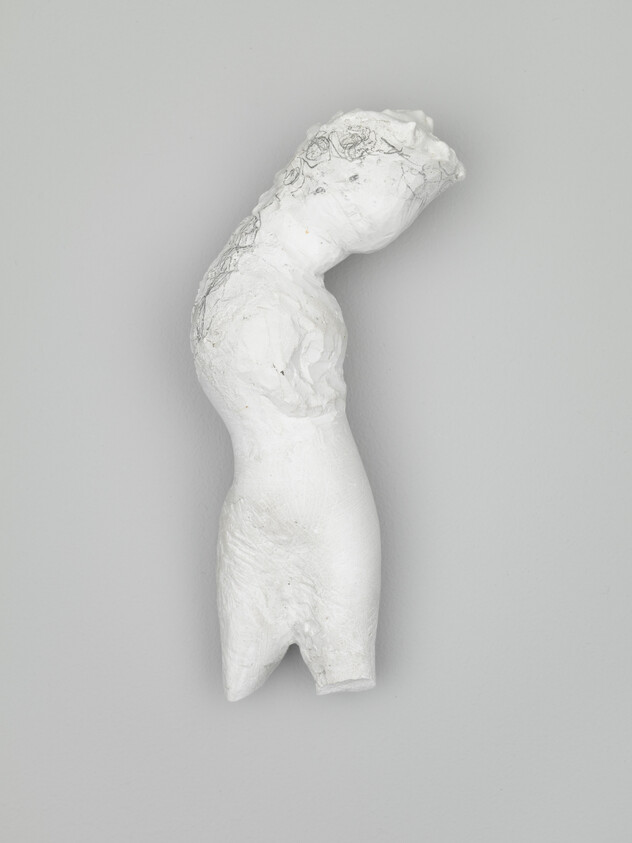 White plaster sculpture of a curved partial human torso mounted on a gray wall.