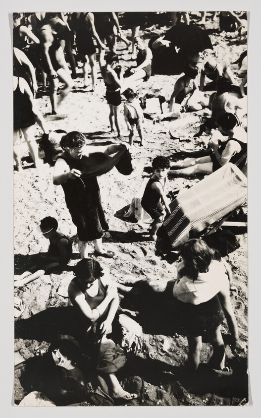 Crowded beach with people and children in vintage swimsuits sitting, standing, and playing on the sand.