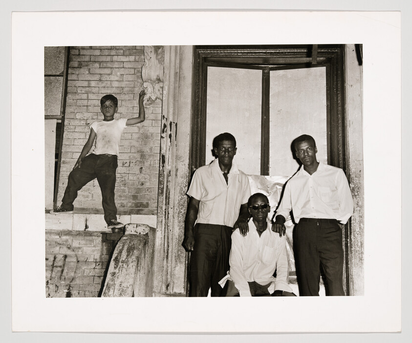 Three men stand in a doorway while a boy poses on a nearby brick ledge.