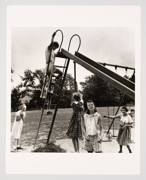 Children gather around a metal slide as one child climbs the ladder and others wait nearby.