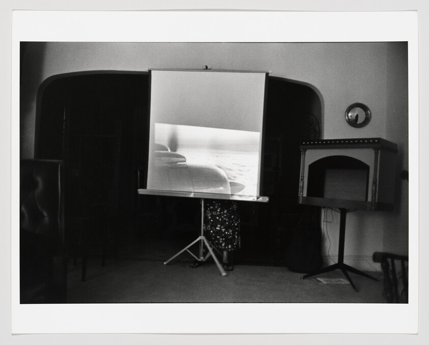 A projection screen showing a film while a person stands partially hidden behind it.