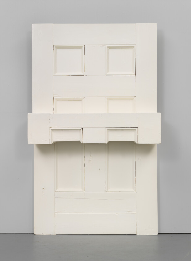 Two white wooden door panels stacked against a gray wall with a narrow shelf between them.