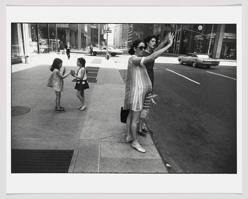 Pregnant woman with sunglasses hails a car at a city curb while children play nearby.