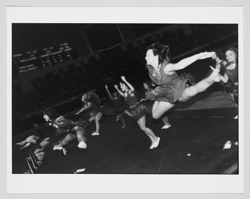 A group of cheerleaders leap in unison across a gym floor during a spirited routine.