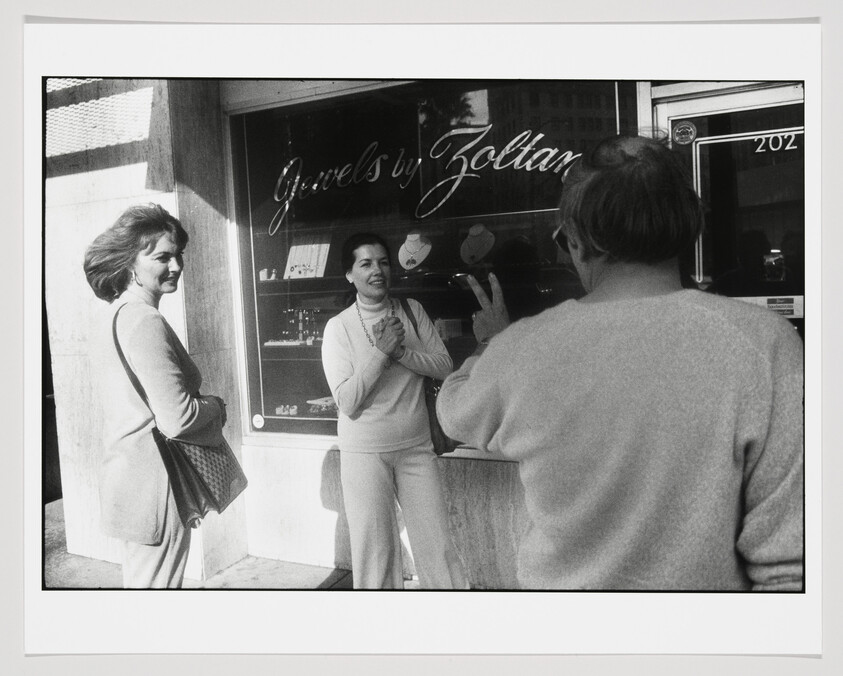 Three people stand smiling outside a jewelry store called Jewels by Zoltan, one man gesturing.