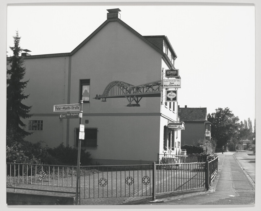 Corner building with a painted bridge mural and a small restaurant sign on a quiet street.