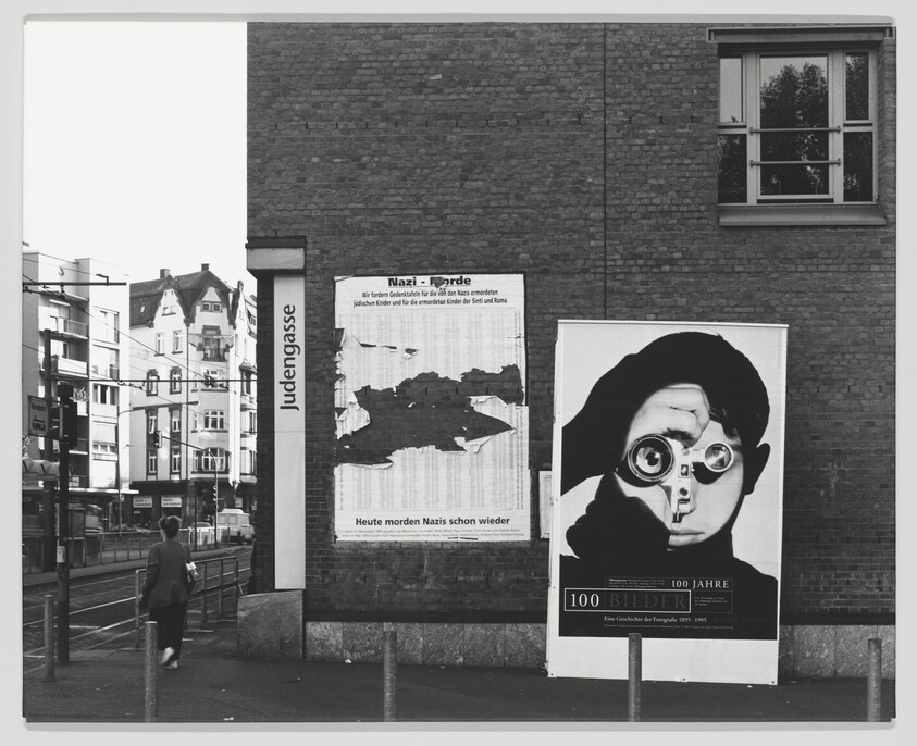 A large poster of a person peering through binoculars on a brick wall by Judengasse.