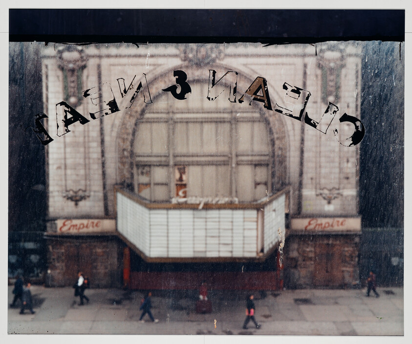 View through a dirty window showing the closed Empire theater marquee with people walking by.