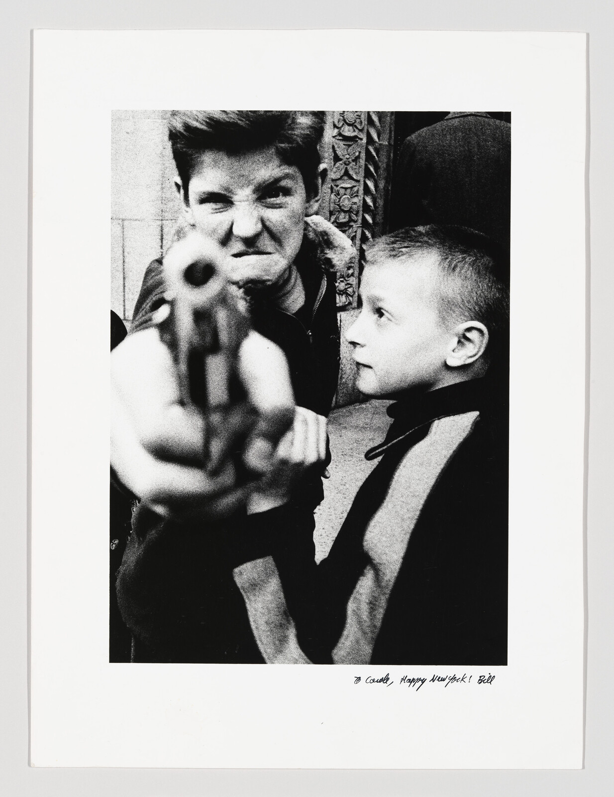 A boy angrily points a toy gun toward the camera while another boy watches.