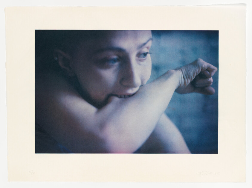 A person bites their forearm while looking pensively to the side in soft blue light.