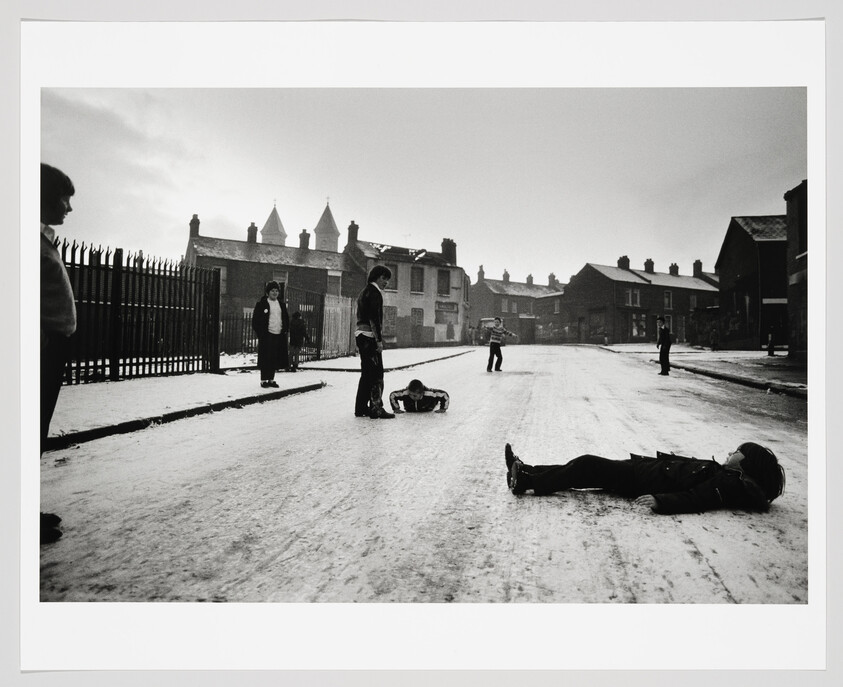 Children play and lie on a snow-covered street in a quiet residential neighborhood.