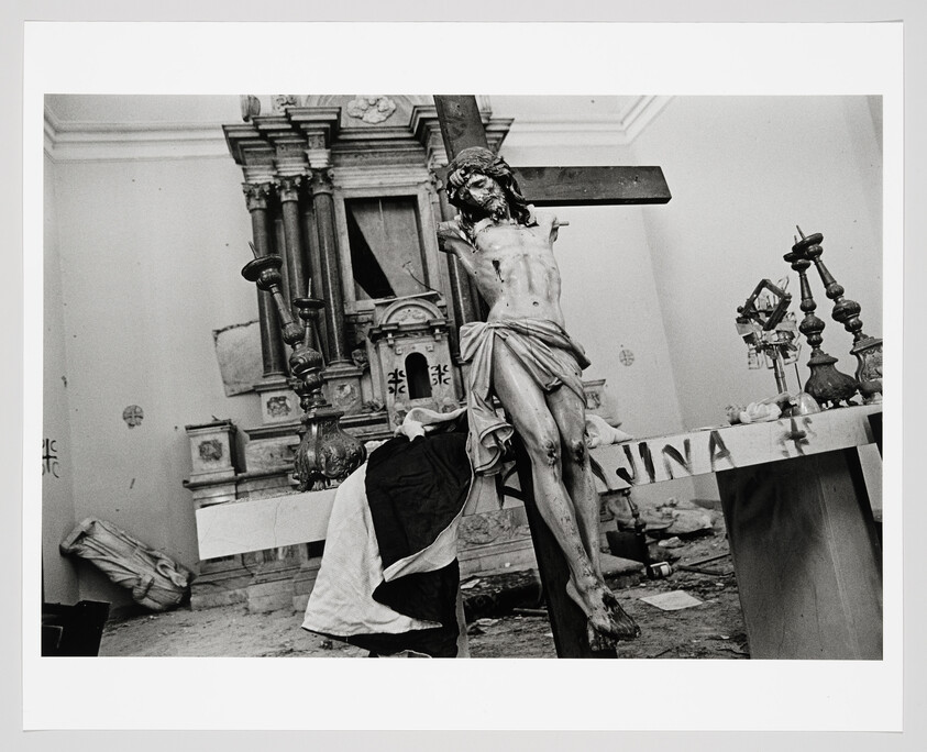 A large crucifix of Jesus leans against a damaged church altar amid scattered debris.