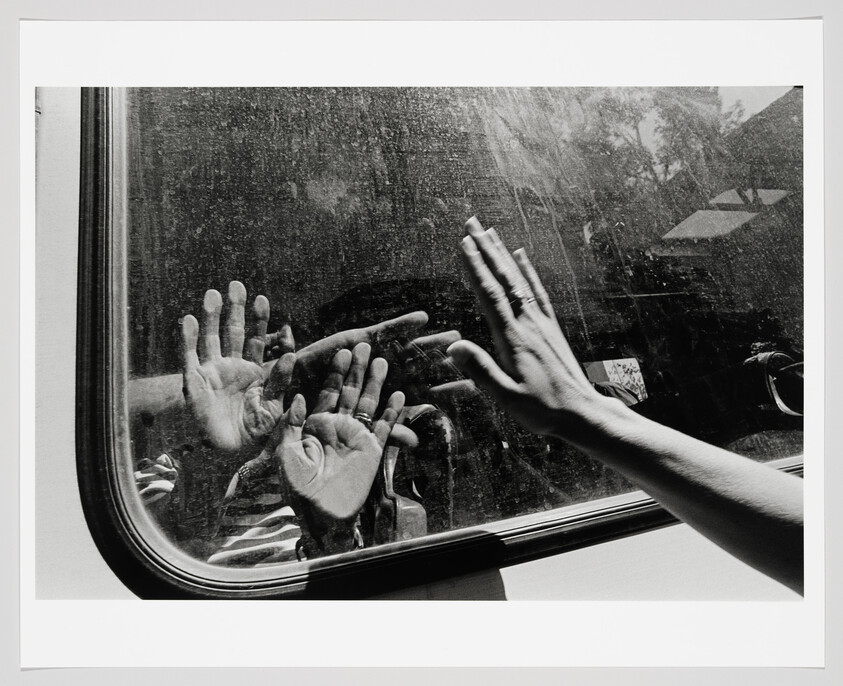Hands pressed against a smudged window with reflected hands reaching toward each other.