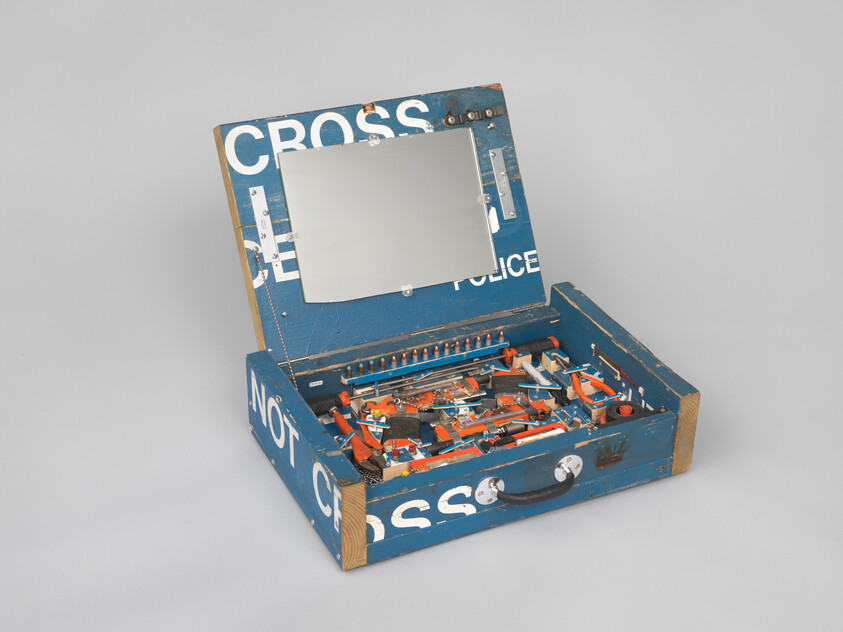 Blue wooden toolbox repurposed from police tape marked 'Do Not Cross' holds many toy tools and a mirror.
