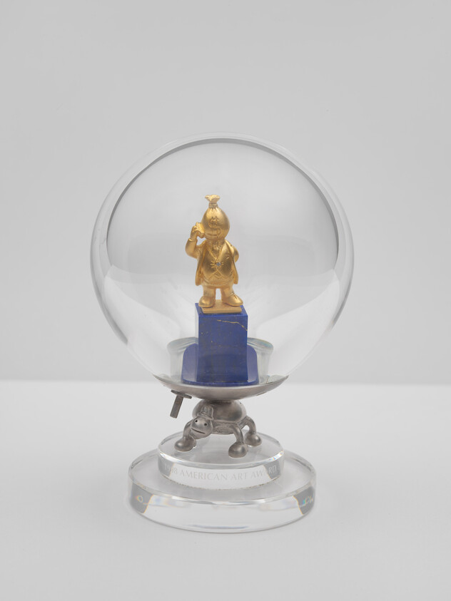 A small gold figurine stands on a blue plinth inside a clear glass globe on a pedestal.