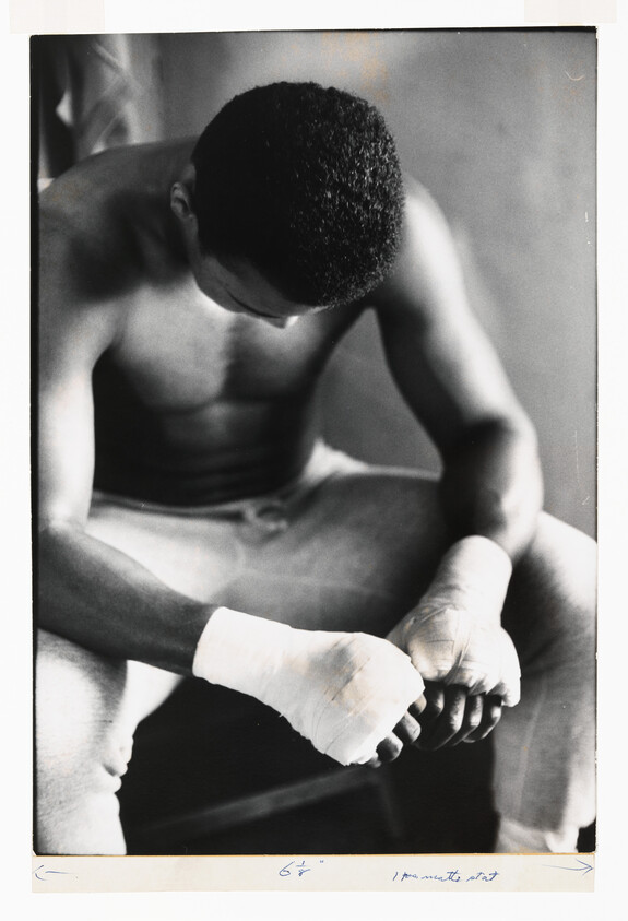 Young boxer with wrapped hands sitting hunched forward, head bowed.