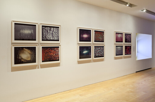 A gallery wall displaying three groups of four framed abstract photographs in a minimalist white room.