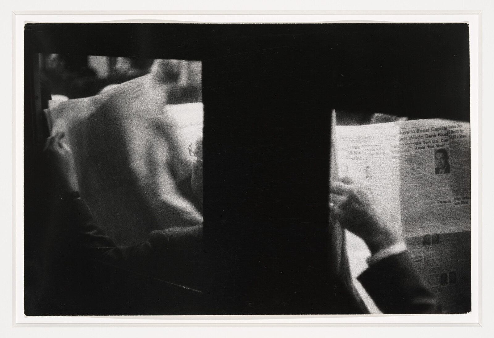 Two people sit reading newspapers on either side of a dark central divider.