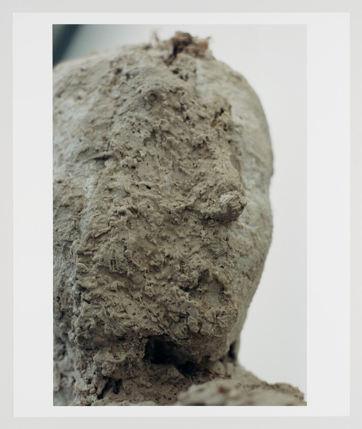 Close-up of a rough, clay-like sculpted human head with heavy textured surface.