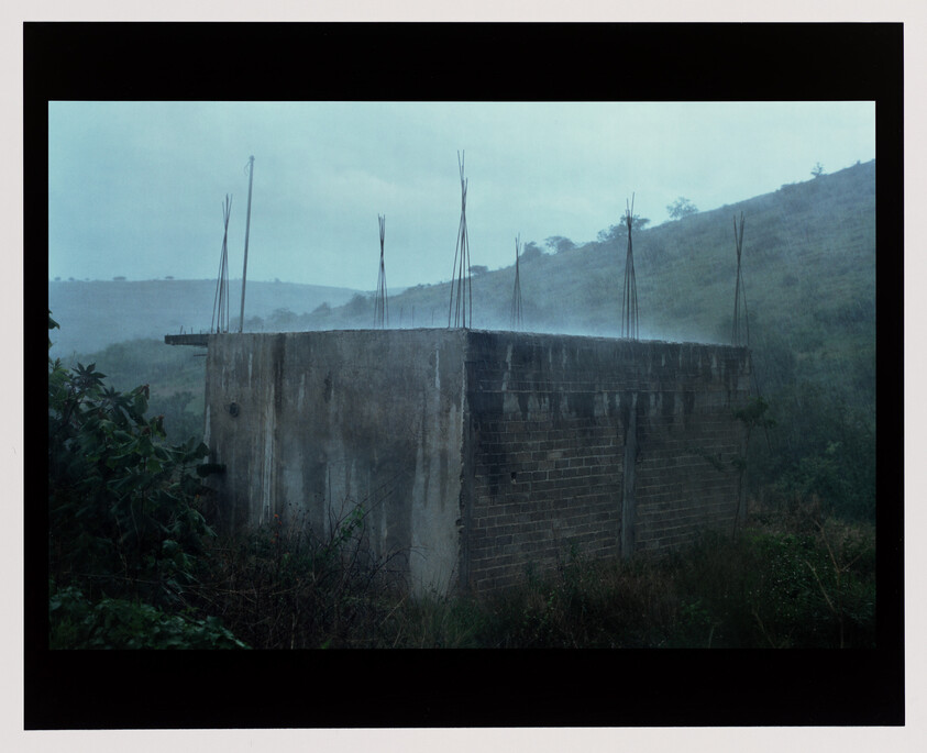 An unfinished concrete building with exposed vertical rebar stands on a misty hillside surrounded by vegetation.