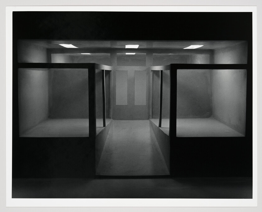 Empty dimly lit room with symmetrical display cases and a central walkway leading to a back wall.