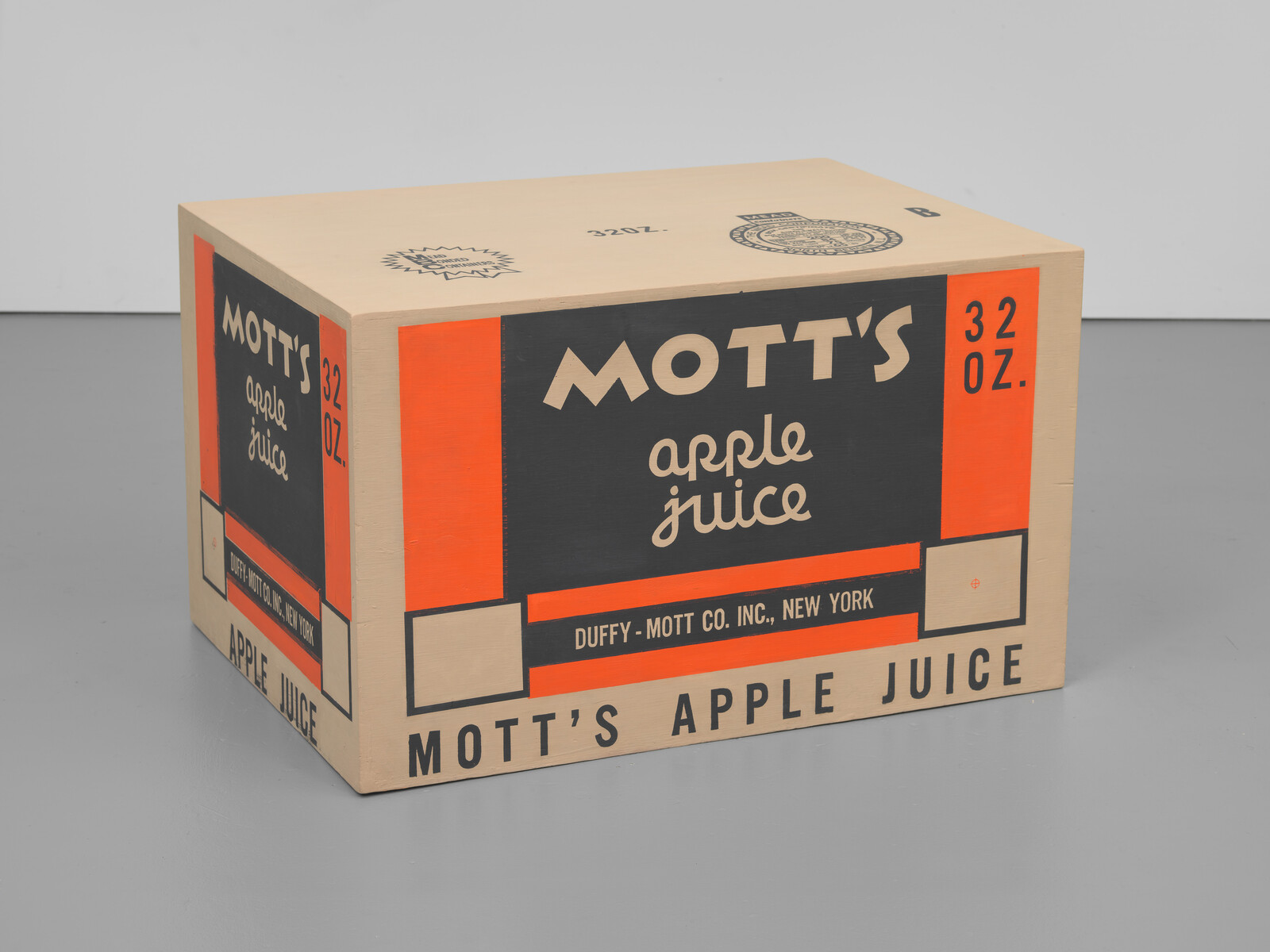 A vintage Mott's apple juice box with a capacity of 32 ounces, featuring bold black, orange, and white design elements, and text indicating the brand and quantity. The box is placed on a grey surface against a light background.