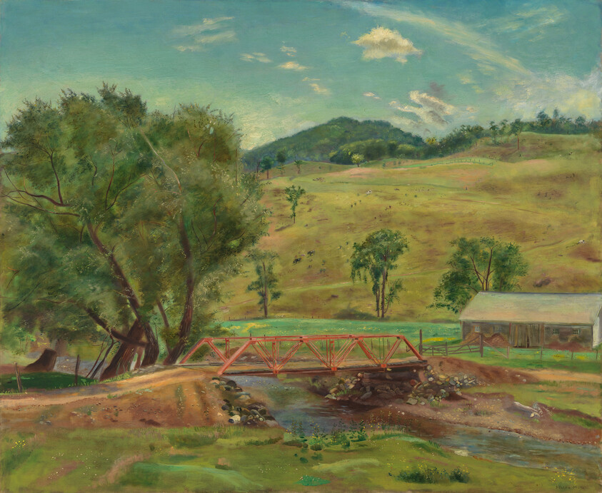 Red wooden bridge over a stream with trees, barn, and rolling green hills.