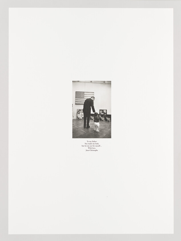 A black and white photograph centered on a white background featuring an adult holding hands with a small child in a room with an American flag and photographs on the wall. Below the image is a caption that reads, "To my father, You were like God, but let me see for myself... Jean Christophe."