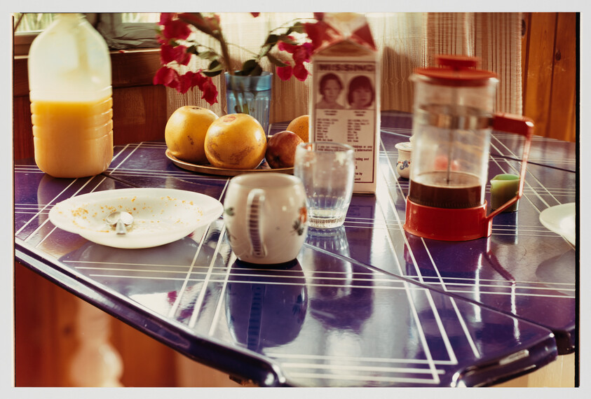 A breakfast table with a French press, mug, glass, orange juice and a plate with crumbs.