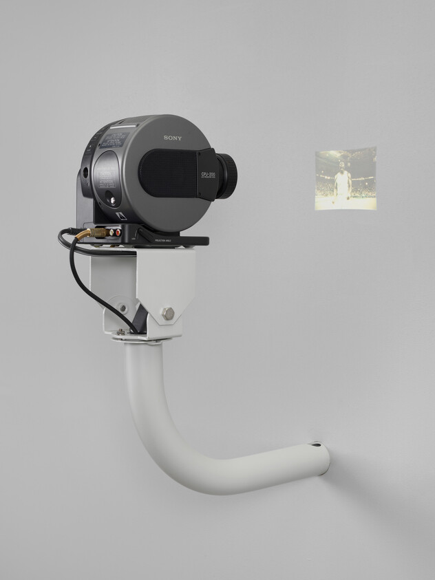 A Sony film projector mounted on a curved white wall bracket projecting a small photograph.