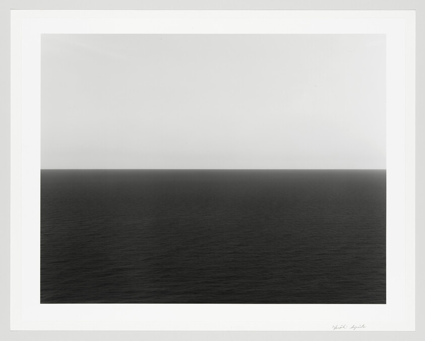 A black-and-white seascape showing a calm dark ocean meeting a pale sky at the horizon.