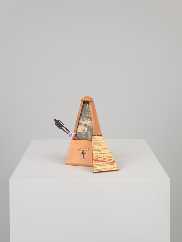 Wooden metronome with a small figure, American flag, and text on a white pedestal.