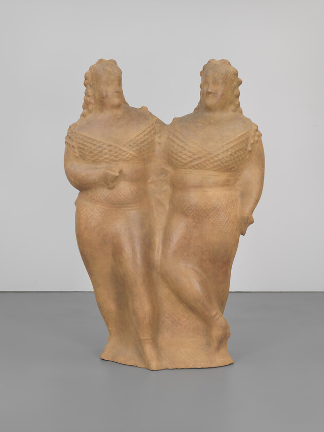 Two conjoined standing female figures in a textured terracotta sculpture with arms at sides and braided hair.