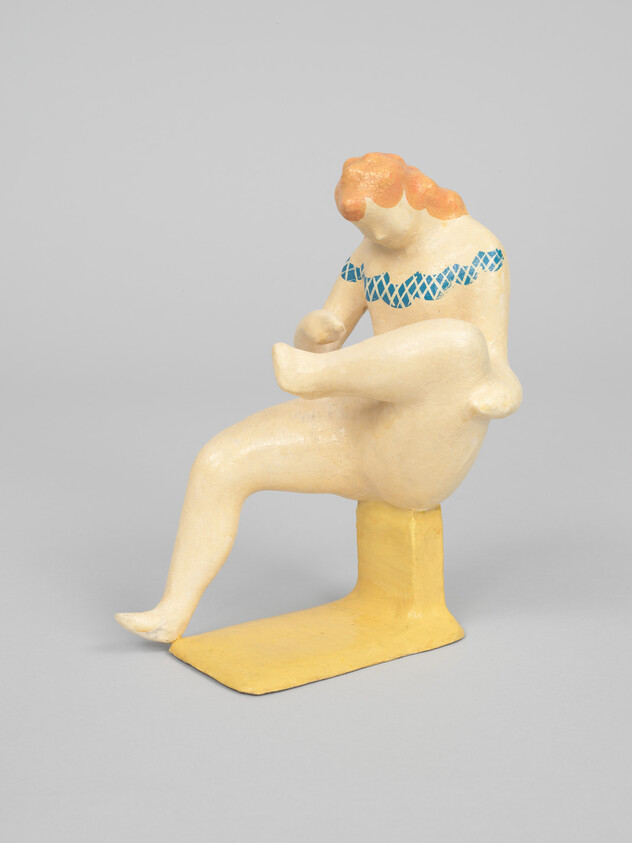 A stylized nude figure with red hair sits on a yellow block holding its raised leg.