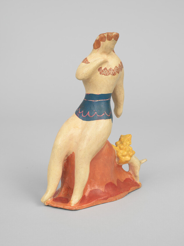 A painted ceramic figure of a seated woman in a blue skirt on an orange rock with a small dog.