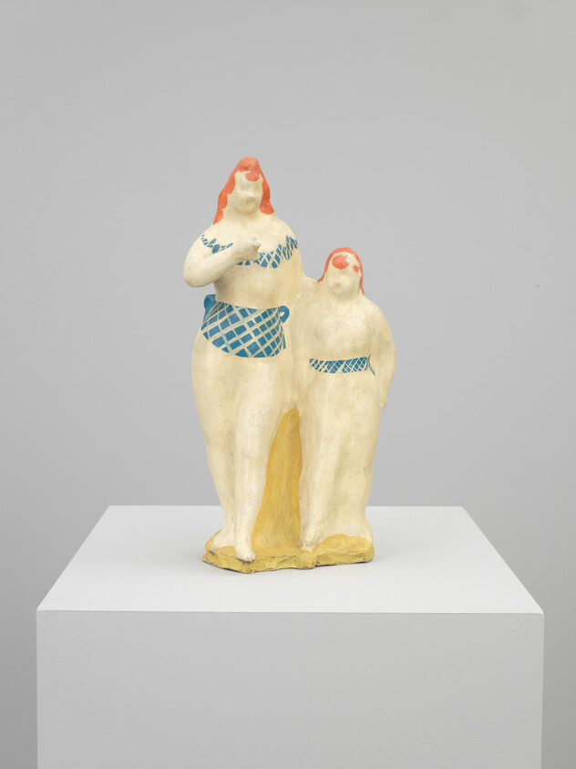 Two stylized cream-colored figures with red hair and blue patterned clothing standing on a white pedestal.