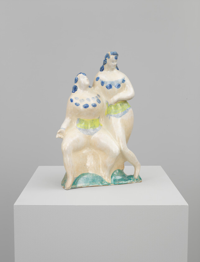 Two stylized ceramic women with blue bead necklaces and green swimsuits posed together on a pedestal.