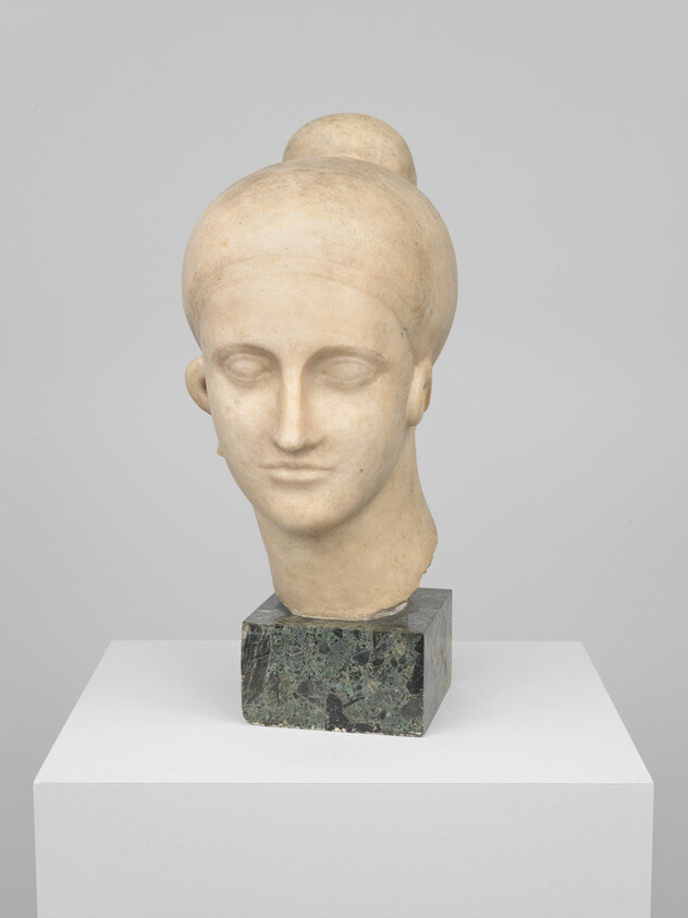 Sculpted marble head of a woman with hair in a bun displayed on a pedestal.
