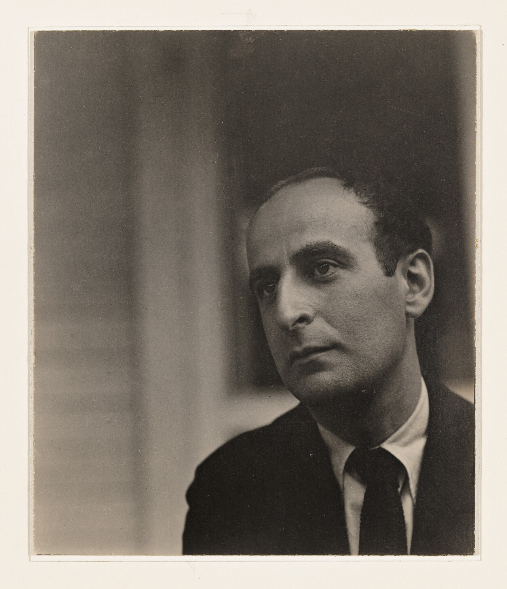 A contemplative man in a suit and tie looks off to the side with a serious expression.