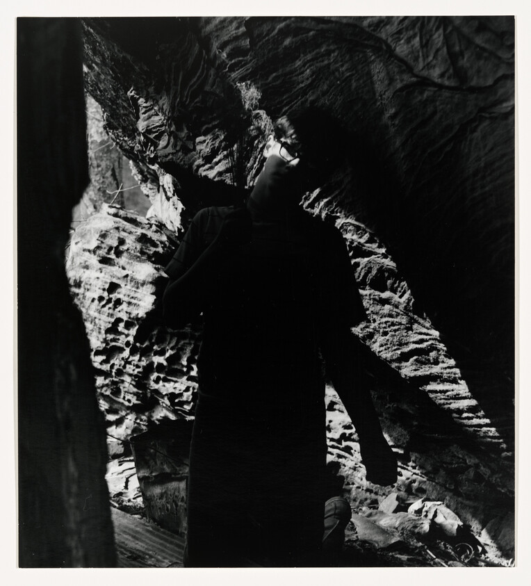 A silhouetted person stands inside a narrow rocky cave with light highlighting textured walls.