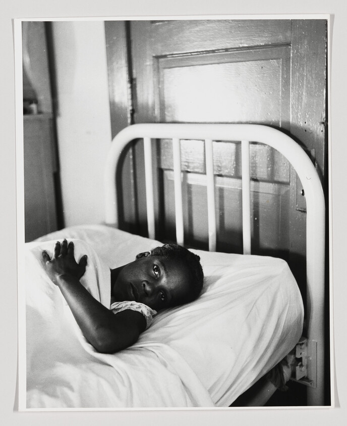 A young woman lies awake in a hospital bed, staring toward the camera.