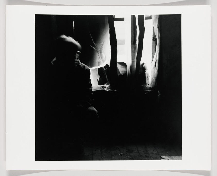 A person sits in shadow beside a torn curtain with bright light streaming through.