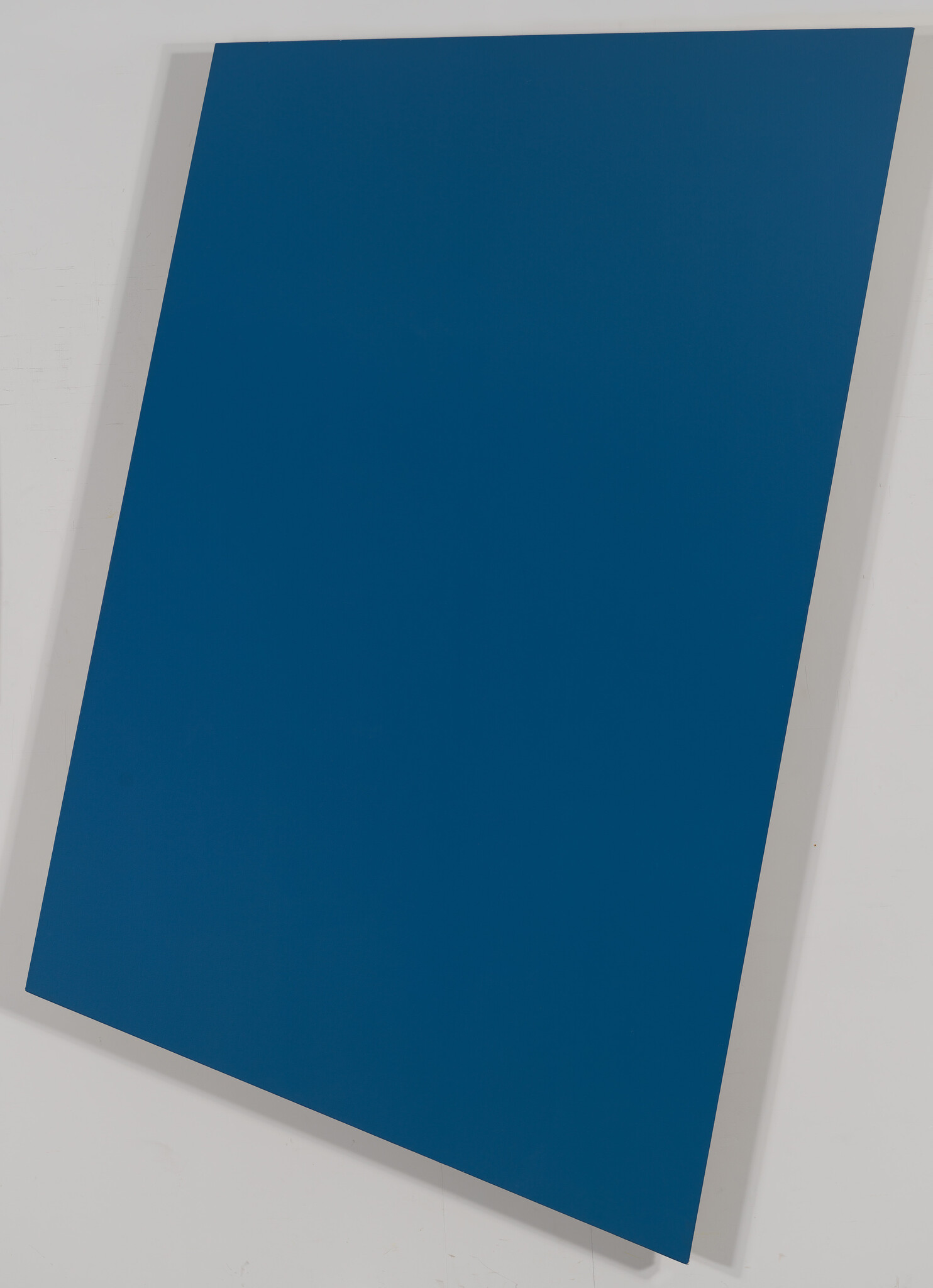 A large tilted rectangular blue panel leaning against a white wall.