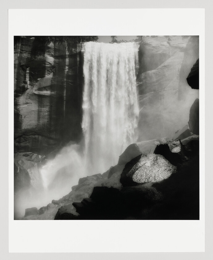 Tall waterfall plunges into a misty pool surrounded by steep rock cliffs and boulders.