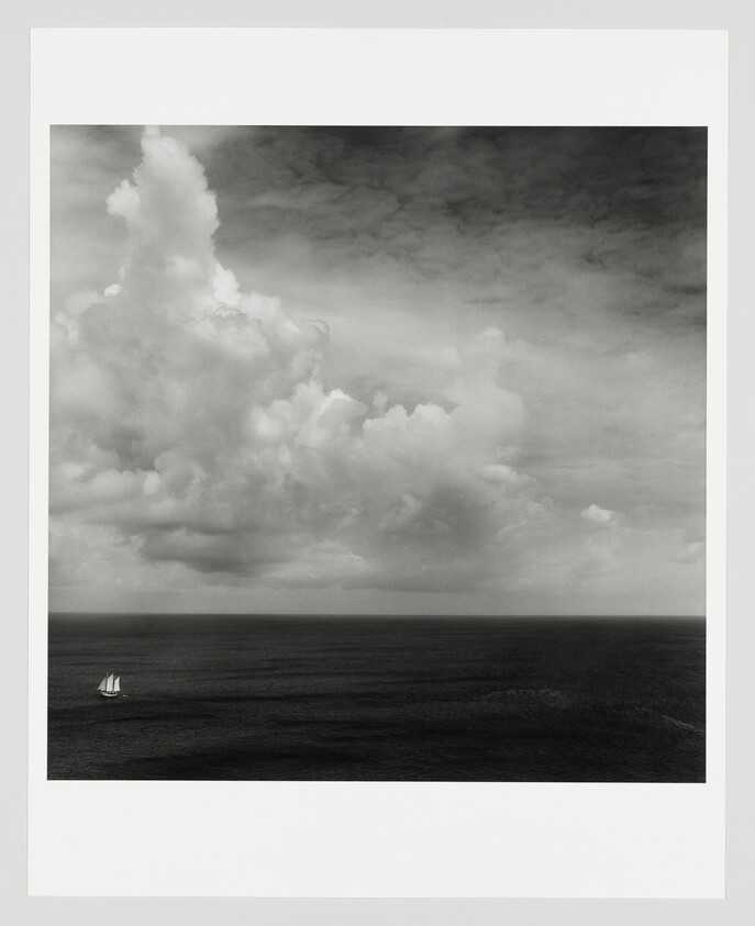 A small sailboat sails across a calm sea under towering cloud formations.