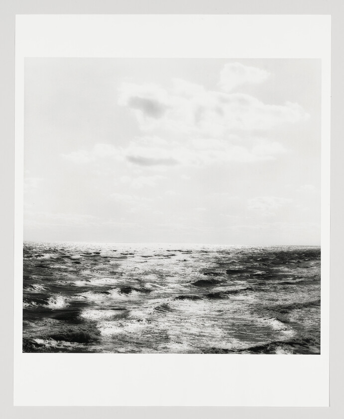 A black-and-white seascape showing choppy waves under a cloudy sky at the horizon.